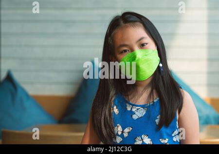 Porträt Asiatische kleine Mädchen trägt eine Gesichtsmaske in einem Restaurant, schwarze lange Haare Kind Mädchen, natürliches Licht aus dem Fenster. Das Konzept für Sicherheit, wenn c Stockfoto