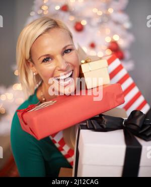 Ich wurde dieses Weihnachten verwöhnt. Porträt einer attraktiven jungen Frau, die ihre Weihnachtsgeschenke hält. Stockfoto