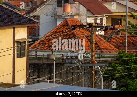 Elektroinstallationsnetz mit Betonmasten auf den Straßen, Seite an Seite mit den Häusern der Menschen in Indonesien, zwischen Energiebedarf und Gefahr Stockfoto