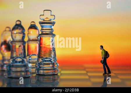 Miniaturfigur Menschen als Geschäftsmann stehen von Angesicht zu Angesicht mit König Schachfigur auf Schachbrett. Hintergrund bei Sonnenuntergang. Stockfoto