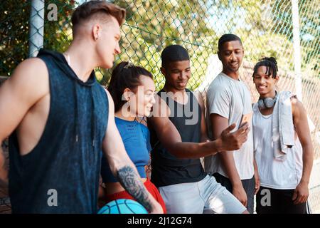 Ihr müsst das sehen. Aufnahme einer Gruppe sportlicher junger Menschen, die auf einem Handy etwas angeschaut haben, während sie an einem Zaun im Freien stehen. Stockfoto