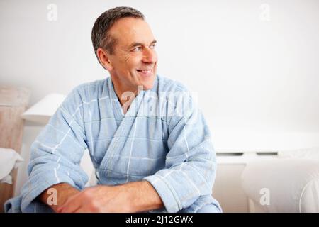 Lächelnder, reifer Mann, der einen Bademantel trägt, während er wegschaut. Nahaufnahme eines lächelnden, reifen Mannes, der einen Bademantel trägt, während er wegschaut. Stockfoto
