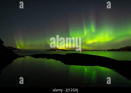 Grüne Nordlichter am Himmel in der Nacht, die sich im Wasser spiegeln Stockfoto