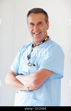Selbstbewusster Arzt mit gefalteten Händen gegen Weiß. Porträt eines lächelnden Arztes mit gefalteten Händen vor weißem Hintergrund. Stockfoto