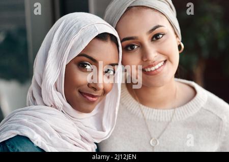 An unseren Wochenenden wird Danke. großartig Beschnittenes Porträt zweier anhänglicher junger Freundinnen, die in Hijab gekleidet in einem Café zusammenhängen. Stockfoto