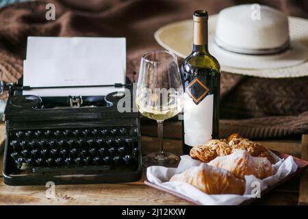 Die Inspiration eines Schriftstellers, der Texte auf einer Vintage-Schreibmaschine schreibt. Freelancer Frühstück Croissants und Wein. Büro im Loft-Stil Stockfoto