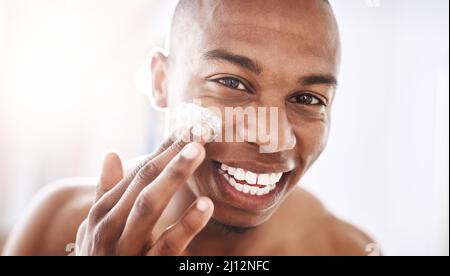 Damen lieben einen sanften Talker mit einem noch glatteren Gesicht. Porträt eines hübschen jungen Mannes, der im Badezimmer zu Hause Feuchtigkeitscreme auf sein Gesicht anwendet. Stockfoto