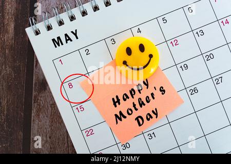 Mai-Kalender auf Holzschreibtisch mit Datumskreis und Text auf Haftnotiz und gelbem Lächeln Gesichtsmagnet. Alles gute zum Muttertag. Stockfoto