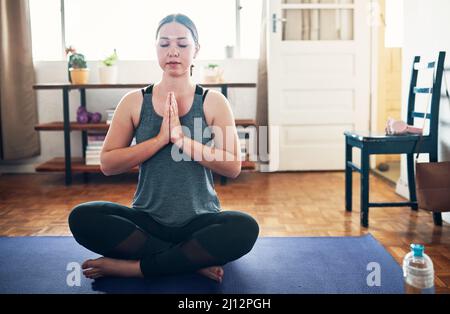 Ich konzentriere mich auf meinen Atem. Eine kurze Aufnahme einer attraktiven jungen Frau, die auf einer Yogamatte sitzt und allein in ihrem Haus meditiert. Stockfoto