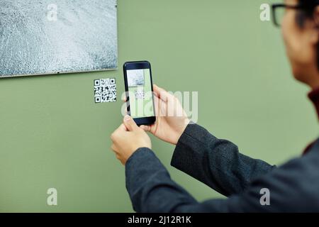 Nicht erkennbarer junger Mann, der Zeit in einer modernen Kunstgalerie verbringt und QR-Code mit seinem Smartphone scannt, um mehr Informationen über Fotos an der Wand zu erhalten Stockfoto