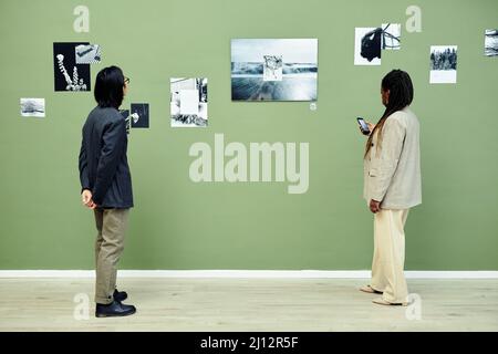 Horizontale Weitwinkelaufnahme eines jungen asiatischen Mannes und einer schwarzen Frau, die Freizeit mit dem Besuch einer modernen Schwarz-Weiß-Fotoausstellung in der Kunstgalerie verbringen Stockfoto