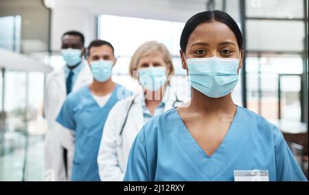 Als medizinisches Fachpersonal haben wir eine so wichtige Aufgabe vor uns. Porträt einer Gruppe von Ärzten, die Gesichtsmasken tragen, während sie zusammen stehen Stockfoto