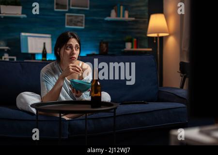 Traurige einsame Frau mit chronischer Depression, die Fernsehsendungen auf dem Bildschirm ansieht, sich verzweifelt fühlt und mit psychischen Problemen zu kämpfen hat. Depressiv ängstlicher Erwachsener, der im Fernsehen einen Film ansieht. Stockfoto