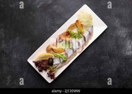 Eingelegter Hering mit gebackenen Kartoffeln, Zwiebeln und Salat auf dunklem Grund Stockfoto