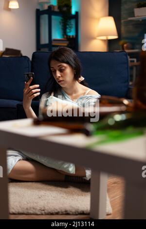 Weibliche Person mit Angst und Depression Surfen im Internet auf dem Smartphone, sitzen auf dem Boden. Suizid depressive Frau, die mit psychischen chronischen Erkrankungen zu tun hat Schwierigkeiten mit dem Handy. Stockfoto
