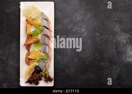 Eingelegter Hering mit gebackenen Kartoffeln, Zwiebeln und Salat auf dunklem Grund Stockfoto