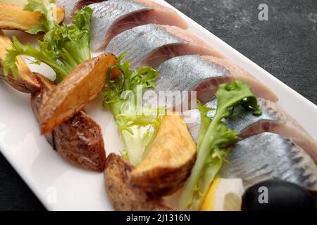 Eingelegter Hering mit gebackenen Kartoffeln, Zwiebeln und Salat auf dunklem Grund Stockfoto