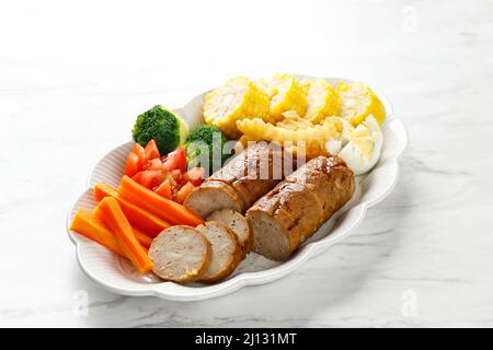 Hackbraten mit Pilzglasur in Scheiben geschnitten auf einem Teller, zermahlenes Rind- und Hühnergericht, serviert mit gedämpftem Gemüse, auf weißem Tisch Stockfoto