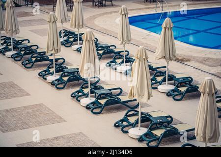 Plastikliegen und Sonnenschirme für den Sonnenschutz sind platziert Auf den Fliesen am Pool im Erholungsgebiet Stockfoto