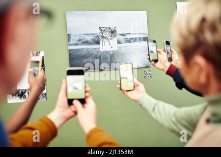 Nicht erkennbare Personen scannen QR-Code mit Smartphones, um mehr Informationen über Fotos an der Wand auf der Ausstellung zu erhalten Stockfoto