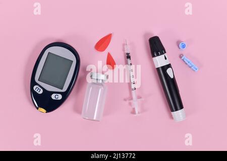 Geräte zur Behandlung von Diabetes mit Blutzucker-Messgerät, Lanzette, Insulinfläschchen und Spritze auf rosa Hintergrund Stockfoto