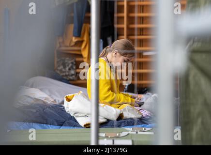 Bad Kreuznach, Deutschland. 21. März 2022. Ein neunjähriges Mädchen aus der Ukraine sitzt auf ihrem Kinderbett in der Notunterkunft in Bad Kreuznach. Das Gymnasium beherbergt derzeit fast nur Flüchtlingsfrauen und -Kinder. (To dpa-Korr 'Horrormomente sind auch in Bad Kreuznach allgegenwärtig') Quelle: Boris Roessler/dpa/Alamy Live News Stockfoto