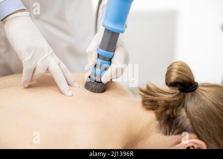 Der Arzt wendet eine Schockwellentherapie auf die Schulter des Mannes an Stockfoto