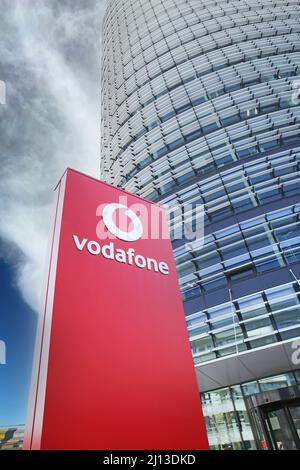 Düsseldorf (Vodafone Campus) – März 9. 2022: Blick auf die rote Säule gegen futuristischen Gebäudeturm und blauen Himmel, flauschige Wolken Stockfoto