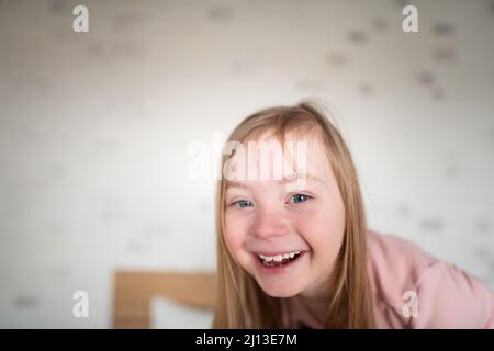 Glückliches kleines Mädchen mit Down-Syndrom, das zu Hause die Kamera anschaut. Stockfoto