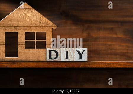 Nahaufnahme eines DIY-Textes aus Holzblöcken (Do IT Yourself) und eines kleinen Holzmodellhauses auf einer Holzwerkbank mit Kopierfläche. Stockfoto