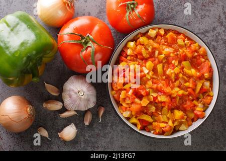 Köstliche sommerliche Sofrito-Sauce aus Paprika, Tomaten, Knoblauch und Zwiebeln in Nahaufnahme auf einem Teller auf dem Tisch. Horizontale Draufsicht von oben Stockfoto