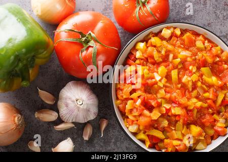 Hausgemachte Soffrito-Sauce aus Paprika, Tomaten, Knoblauch und Zwiebeln in Nahaufnahme auf einem Teller auf dem Tisch. Horizontale Draufsicht von oben Stockfoto