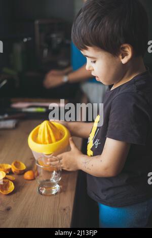 Junge gießt den Saft in das Glas, das nach dem Zusammendrücken von zwei Orangen in die Quetschpresse hergestellt wurde. Frische, gesunde Lebensmittel. Gesunder Lebensstil. Gesunde Ernährung. Vegetarisch Stockfoto