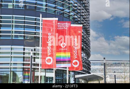 Düsseldorf (Vodafone Campus) – März 9. 2022: Blick auf rote Fahnen am modernen futuristischen Eingang des Verwaltungsgebäudes gegen blauen Himmel Stockfoto