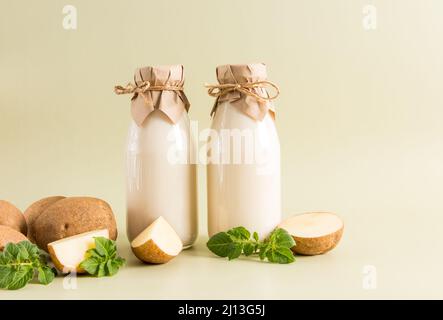 Zwei Glasflaschen mit veganer Pflanzenmilch aus Kartoffelknollen auf beigefarbenem pastellfarbenem Hintergrund. Das Konzept der gesunden Ernährung. Getränkersatz Stockfoto