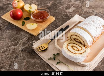 Hausgemachte leckere Biskuitrolle auf einem Holzblech mit Backzutaten auf einem marmorbraunen Hintergrund Stockfoto