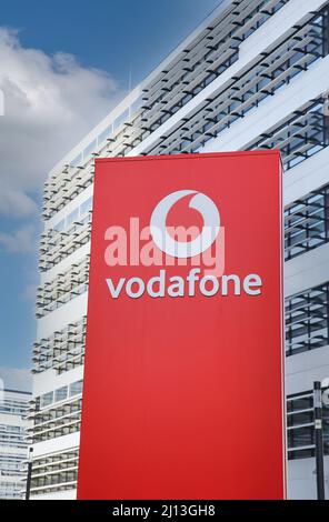 Düsseldorf (Vodafone Campus) – März 9. 2022: Blick auf die rote Säule gegen futuristischen Gebäudeturm und blauen Himmel, flauschige Wolken Stockfoto