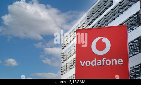 Düsseldorf (Vodafone Campus) – März 9. 2022: Blick auf die rote Säule gegen futuristischen Gebäudeturm und blauen Himmel, flauschige Wolken Stockfoto