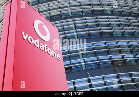 Düsseldorf (Vodafone Campus) – März 9. 2022: Blick auf die rote Säule gegen futuristischen Gebäudeturm und blauen Himmel, flauschige Wolken Stockfoto