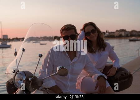 Das Paar genießt einen Urlaub, während es auf einem Motorroller am Meer sitzt und den wunderschönen Sonnenaufgang genießt. Selektiver Fokus Stockfoto