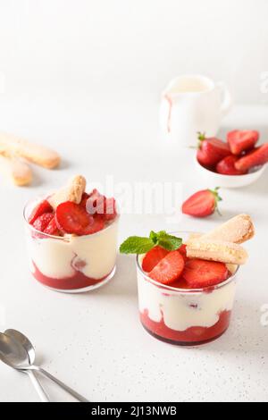 Mehrlagiges Dessert in Gläsern mit Keksen, Mascarpone-Käse und Schlagsahne auf weißem Hintergrund. Italienische Tiramisu mit Erdbeeren. Stockfoto