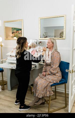 Kosmetikerin, die Foundation Make-up auf eine blonde Frau in einem Schminkstuhl anwendet Stockfoto