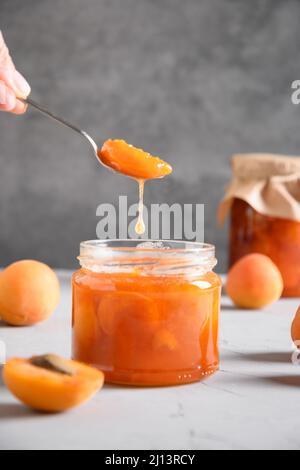 Hausgemachte Aprikosenmarmelade oder Marmelade im Löffel auf grauer Küchentifläche. Saisonale Konserven. Nahaufnahme. Vertikales Format. Stockfoto