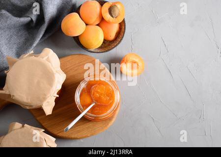 Aprikosenmarmelade in Gläsern und Früchte auf grauem Hintergrund. Konserven. Blick von oben. Speicherplatz kopieren. Stockfoto