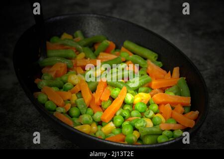 Gemischtes Gemüse, Erbsen, Karotten, grüne Bohnen und Mais, in einer schwarzen Schale.. Auf einem schwarzen Steingrund Stockfoto