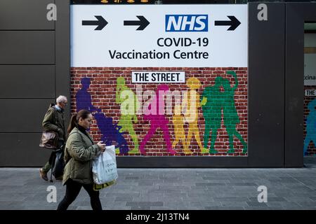 London, Großbritannien. 22. März 2022. Die Menschen passieren ein Schild zu einem Covid-19 Impfzentrum in Stratford, im Osten Londons. Es wird berichtet, dass die Covid-19-Fälle zunehmen, da eine neue Covid-19-Variante entstanden ist und im Herbst eine vierte Impfung angeboten werden könnte.Quelle: Stephen Chung / Alamy Live News Stockfoto