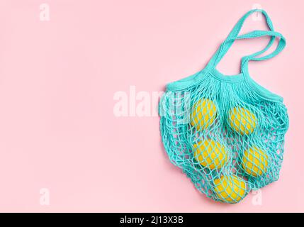 Zitronen in Netztasche auf rosa Hintergrund. Null-Verschwendung beim Einkaufen. Stockfoto