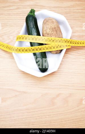 Biodynamische ökologische Landwirtschaft und Ernährung Konzept - frische gesunde Zucchini und Kartoffeln in einer weißen Keramikplatte auf Holztisch mit Platz für Text Stockfoto