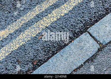 Nahaufnahme von doppelten gelben Linien auf einer getrackten Straße und Bordsteinen, diagonal Stockfoto