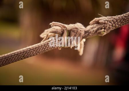 Nahaufnahme eines Schnitts und ausgefransten Seils, um mit verschwommenem Hintergrund zu brechen und Raum zu kopieren. Horizontal. Konzept der Probleme, Stress. Stockfoto